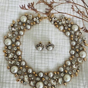 Peut inclure: Un collier ras de cou et des boucles d'oreilles assorties en ton or avec de fausses perles et des strass transparents.
