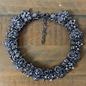 May include: A black statement necklace with a large, ornate design featuring black and clear rhinestones.