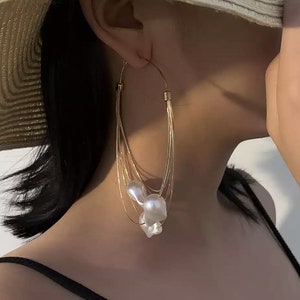 May include: Gold hoop earrings with multiple strands of chain and a cluster of white pearl-like beads.
