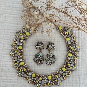 May include: A yellow and white statement necklace and matching earrings with a geometric design. The jewelry is made of metal and features a variety of clear and yellow rhinestones.