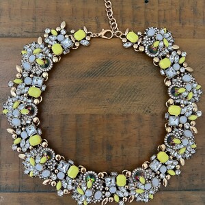 May include: A yellow and white statement necklace with a gold chain and a large cluster of rhinestones and faceted glass stones.