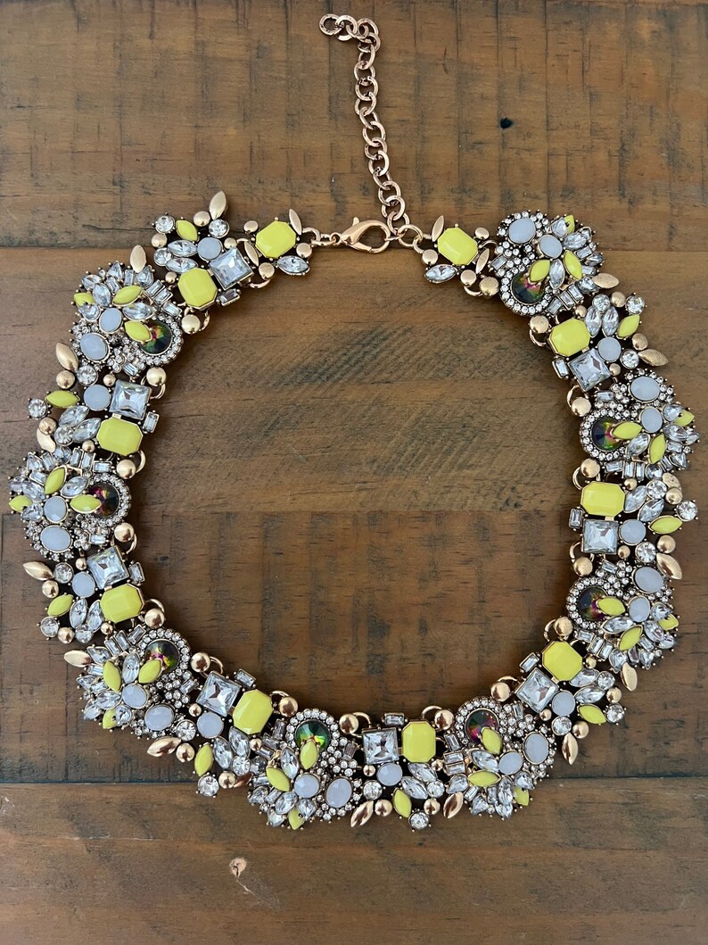 May include: A yellow and white statement necklace with a gold chain and a large cluster of rhinestones and faceted glass stones.