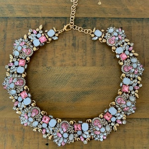 May include: A gold tone statement necklace with pink and white rhinestones. The necklace is made of metal and has a chain closure.