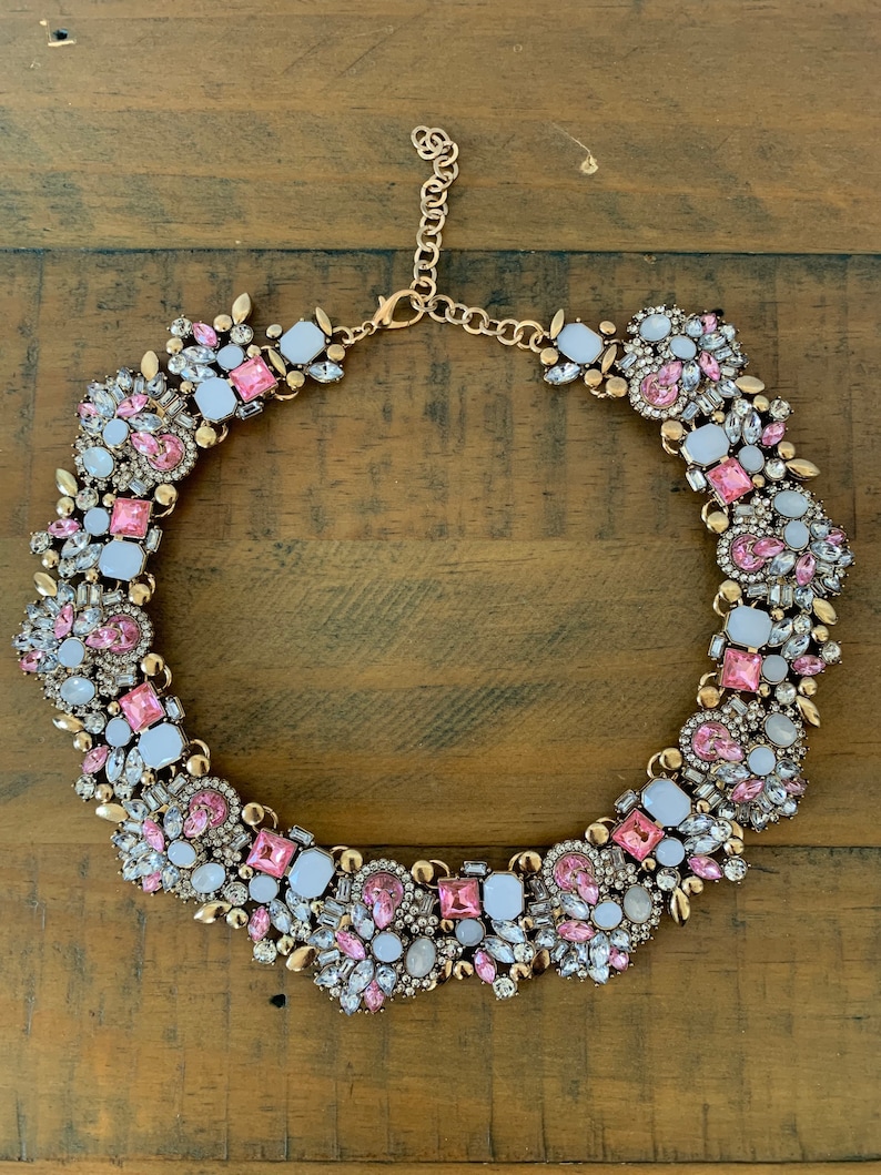 May include: A gold tone statement necklace with pink and white rhinestones. The necklace is made of metal and has a chain closure.