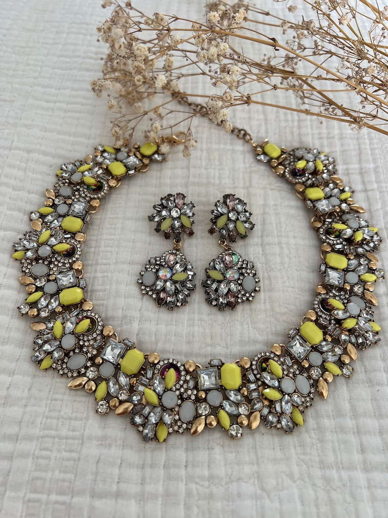 May include: A yellow and gold statement necklace and matching earrings with a cluster of rhinestones and yellow stones.