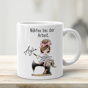 Könnte beinhalten: Weiße Keramiktasse mit einer bunten Illustration eines Mädchens, das auf einer Nähmaschine sitzt. Der Text "Nähfee bei der Arbeit" und der Name "Aylin" sind auf die Tasse gedruckt.