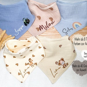 Könnte beinhalten: Verschiedene Baby-Lätzchen in Blau, Rosa und Creme. Jedes Lätzchen hat ein einzigartiges Design, darunter ein Traktor, Regenbogen, Herzen, ein Pferd und ein Teddybär. Auf einigen Lätzchen sind Namen aufgedruckt. Die Lätzchen sind aus weichem Stoff.