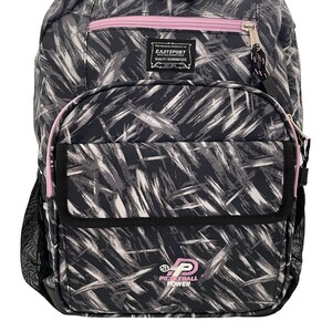 May include: Black and white patterned backpack with pink accents. The backpack has a large main compartment, a front pocket, and two side mesh pockets. The front pocket has a black patch with the text "Eastsport" and "Quality Guaranteed". The bottom of the backpack has a black patch with the text "Pickleball Power" and a pickleball logo.