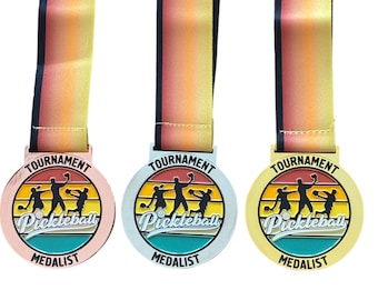 May include: Three pickleball tournament medals with a retro sunset design. The medals are gold, silver, and bronze. Each medal has the words "Tournament Medalist" and "Pickleball" on it.