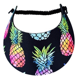 May include: Black visor featuring a repeating pattern of colorful watercolor pineapples. The pineapples have a gradient of pink, yellow, green, and blue. The visor has a black elastic band.