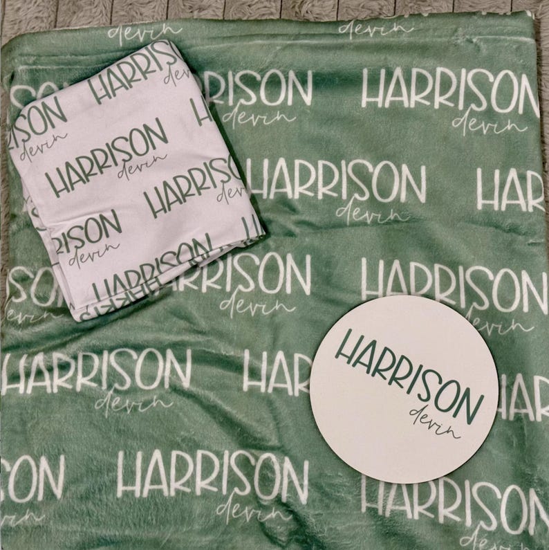K&ouml;nnte beinhalten: Eine salbeigr&uuml;ne Pl&uuml;schdecke mit einem sich wiederholenden wei&szlig;en Muster des Namens Harrison Devin, ein gefaltetes wei&szlig;es Stoffquadrat mit demselben gr&uuml;nen Text und eine runde wei&szlig;e Holzscheibe, die mit dem Namen Harrison Devin in Gr&uuml;n bedruckt ist.