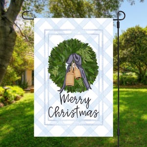 May include: A garden flag with a blue and white checkered background. The flag features a green wreath with a gray bow and two gold bells. The words "Merry Christmas" are written in black script.