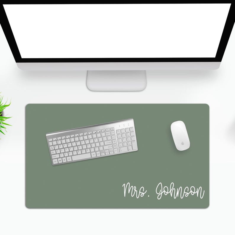Puede incluir: Una alfombrilla de escritorio verde salvia con teclado y rat&oacute;n blancos. La alfombrilla tiene el nombre "Mrs. Johnson" en fuente cursiva. El teclado es plateado y tiene un juego completo de teclas. El rat&oacute;n es blanco y tiene un dise&ntilde;o minimalista.