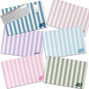 May include: A collection of rectangular mouse pads with vertical stripes in various pastel colors, including blue, pink, purple, and green. Each pad features the initials "JKF" in the bottom right corner. A keyboard and mouse are on one of the blue striped pads.