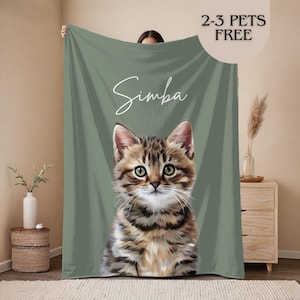 May include: A green blanket with a detailed illustration of a tabby kitten. The kitten's name, "Simba," is written in cursive. The blanket also has the text "2-3 PETS FREE" in a circular design.