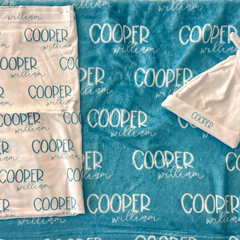 K&ouml;nnte beinhalten: Eine wei&szlig;e Puckdecke und eine passende wei&szlig;e Babym&uuml;tze, beide mit den in T&uuml;rkis gedruckten Namen Cooper und William. Diese Artikel liegen auf einer t&uuml;rkisfarbenen Decke, die ebenfalls die Namen Cooper und William in wei&szlig;em Text zeigt.