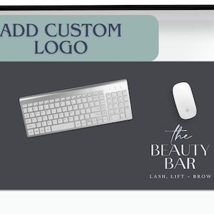 May include: A dark gray rectangular desk mat with a silver keyboard and white mouse. The mat features the text "the BEAUTY BAR" with "LASH, LIFT + BROW" below. Above the mat is a light blue rectangle with the text "ADD CUSTOM LOGO".