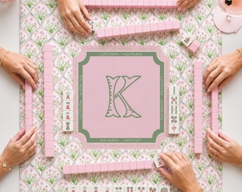 以下が含まれることがあります： ピンクの花柄のプレイマットに、大きな緑色の文字Kと「PLAY RIGHT」「WALLS LEFT」というテキストが中央の四角形に配置された麻雀ゲームセット。ピンクの牌と、赤と緑のシンボルが描かれた白い牌が含まれています。