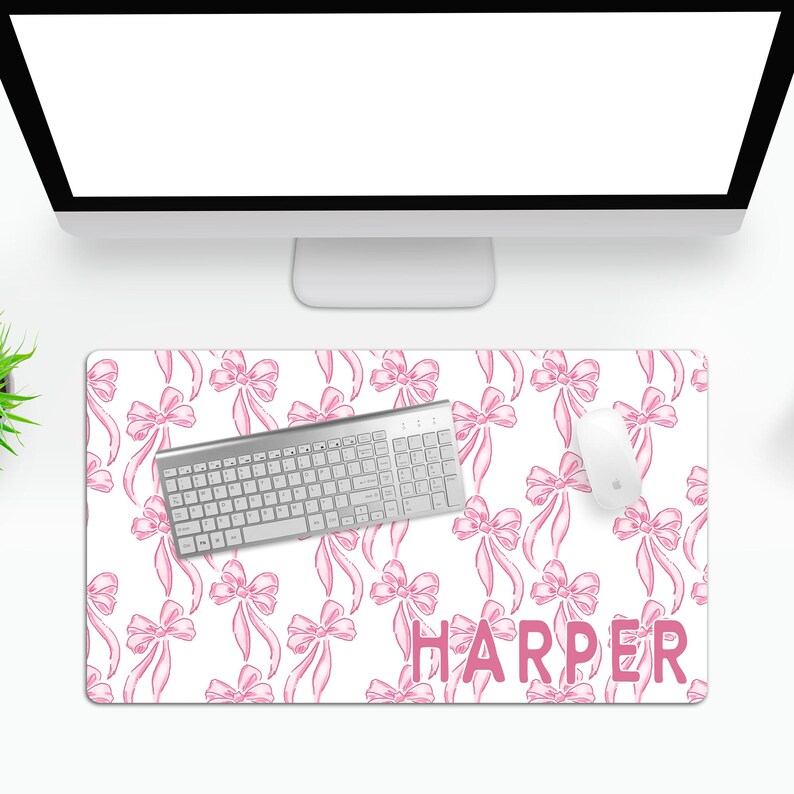 May include: White desk mat with a pink bow pattern and the name "HARPER" in pink letters. A silver keyboard and a white mouse are on the mat.