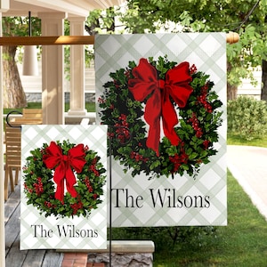 May include: Two outdoor garden flags featuring a Christmas wreath design with a large red bow and red berries. The flags have a green and white plaid background and the text "The Wilsons".