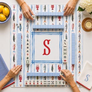 May include: A square mahjong mat featuring a white background with blue vertical stripes and a repeating pattern of colorful lobsters and fish. The center displays a large red letter S. The mat includes light blue tile racks and mahjong tiles.