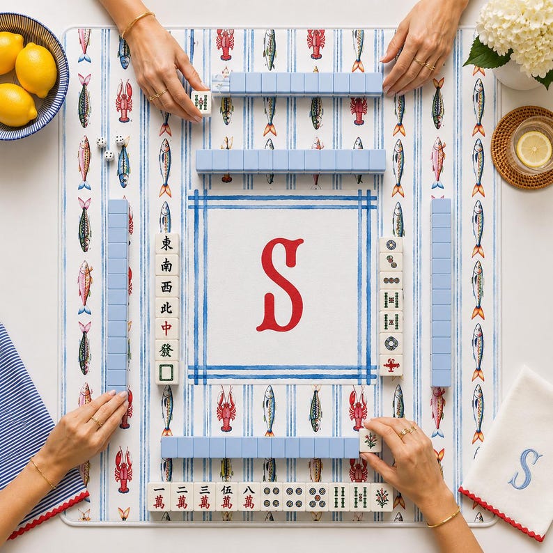May include: A square mahjong mat featuring a white background with blue vertical stripes and a repeating pattern of colorful lobsters and fish. The center displays a large red letter S. The mat includes light blue tile racks and mahjong tiles.