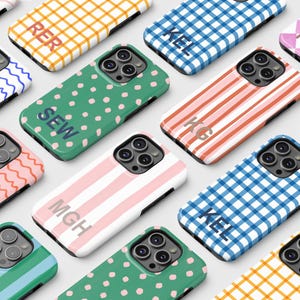 May include: A collection of smartphone cases with various patterns and colors. Designs include stripes, polka dots, wavy lines, and checkered patterns. Each case has a unique initial or monogram. The cases are in shades of pink, green, blue, and yellow.