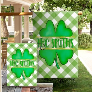 May include: A garden flag featuring a green and white gingham check pattern with a large green four-leaf clover in the center. The text THE SMITHS is printed in green across the middle of the clover, separated by a thin gold horizontal line.