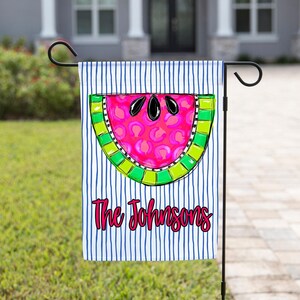 May include: A rectangular garden flag featuring a white background with vertical navy blue stripes. Centered is a watermelon slice with a pink leopard print interior, a bright green rind, and black seeds. The text The Johnsons is in pink.