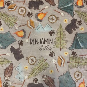 May include: Gray fabric with a camping theme, featuring illustrations of bears, tents, compasses, s'mores, and trees. The text "BENJAMIN phillip" is printed in the center. The design includes paw prints, owls, and campfires.