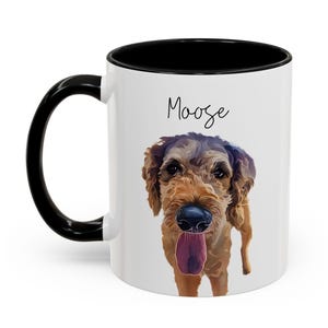 May include: White ceramic mug with a black handle and rim. The mug features a portrait of a dog with brown fur and a pink tongue, and the name "Moose" in black script.