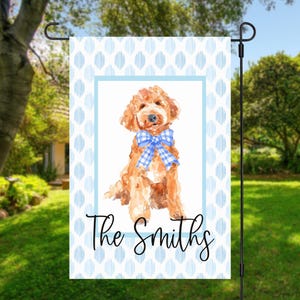 May include: A rectangular garden flag featuring a watercolor illustration of a golden-brown dog wearing a blue and white gingham bow. The background has a light blue and white vertical pattern, and the text The Smiths is written in black.