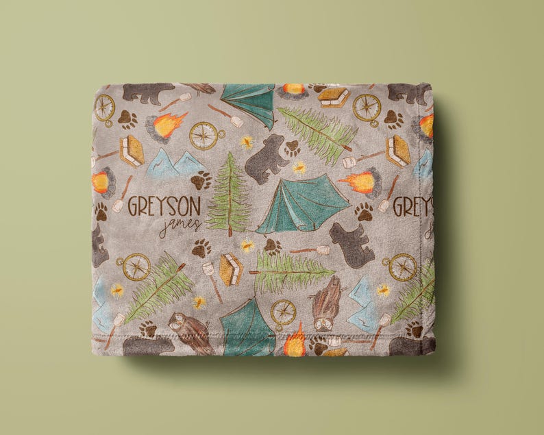May include: A gray blanket with a camping-themed pattern. The design includes bears, tents, compasses, campfires, trees, and paw prints. The blanket has the names "Greyson" and "Grey" printed on it.