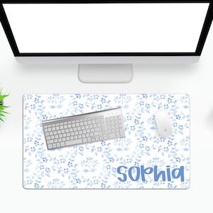 May include: A rectangular desk mat featuring a light blue and white watercolor floral pattern with small leaves and berries. The name Sophia is printed in a bold, blue, rounded sans-serif font in the bottom right corner of the mat.