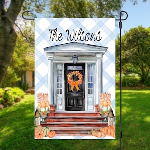 May include: A rectangular garden flag featuring a light blue and white buffalo check background with the text The Wilsons. The illustration depicts a black front door with a fall wreath, white columns, red brick steps, and orange pumpkins.