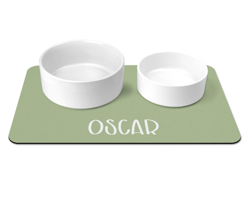 May include: A green pet food mat with the name "Oscar" printed on it. Two white ceramic bowls are on the mat.