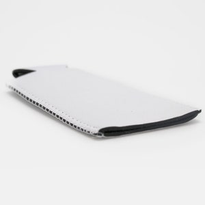May include: A white neoprene phone sleeve with a black trim and stitched edge. The sleeve is rectangular and designed to protect a smartphone. The product is shown on a white background.