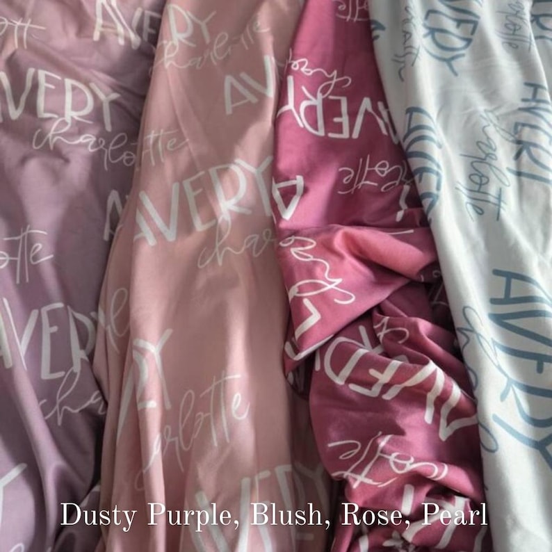 May include: Close-up of four fabric swatches in dusty purple, blush, rose, and pearl. Each fabric is printed with the name "AVERY" and "charlotte" in a white script font. The fabrics are folded and draped, showcasing their textures.