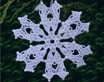 May include: White crocheted snowflake ornament with a delicate design. The snowflake is hanging from a white ribbon against a green background.