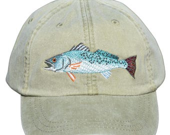 May include: A khaki baseball cap with an embroidered image of a speckled trout fish.