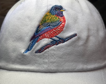May include: White baseball cap with an embroidered colorful bird perched on a branch.