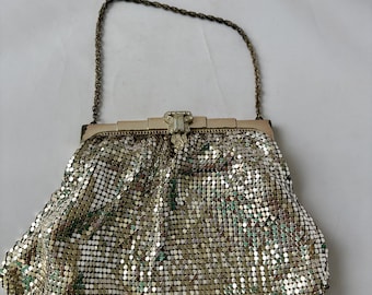May include: A vintage silver mesh handbag with a chain handle. The bag features a decorative clasp and is made of small, reflective metal squares. The bag is approximately 8 inches wide.