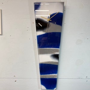 May include: A blue, white, and silver abstract resin clock with gold hands. The clock is shaped like a long, thin triangle.