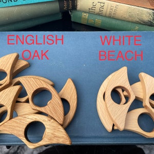 Op de afbeelding: Twee sets houten ringhouders, &eacute;&eacute;n set is gemaakt van Engelse eik en de andere van wit strandhout. Beide sets zijn in een cirkelvormige opstelling.