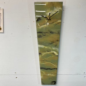May include: A green, white, and black abstract clock with a long, narrow, rectangular shape. The clock face is white with black hands.