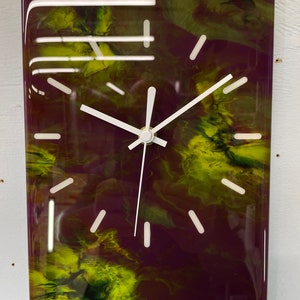 May include: A rectangular clock with white hands and black markings on a purple and yellow abstract background.