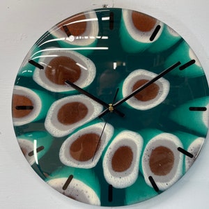 May include: A round clock with a green and white abstract design. The clock face has a swirling pattern of white and brown circles with a black clock hand.
