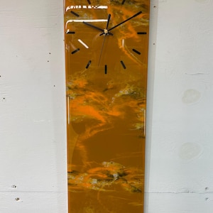 Könnte beinhalten: Eine rechteckige Uhr mit schwarzem Zifferblatt und schwarzen Zeigern. Das Zifferblatt der Uhr ist vor einem Hintergrund aus orangefarbenem, gelbem und weißem Harz mit Marmoreffekt platziert.