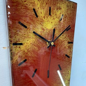 May include: A rectangular clock with black hands and gold accents. The clock face is made of resin and has a red and yellow marbled design.