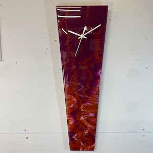 May include: A long, vertical clock with a white face and black hands. The clock is encased in a clear resin with a purple and orange swirl pattern.